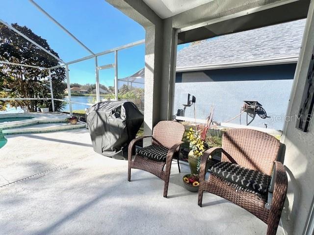 view of patio with a water view, a grill, and a lanai