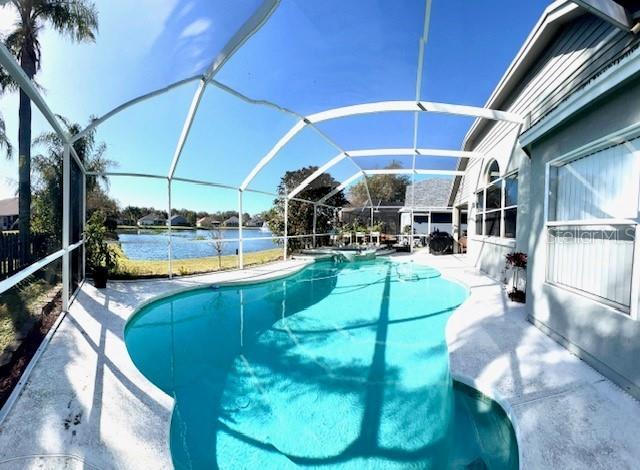 view of swimming pool featuring a patio, a water view, and glass enclosure