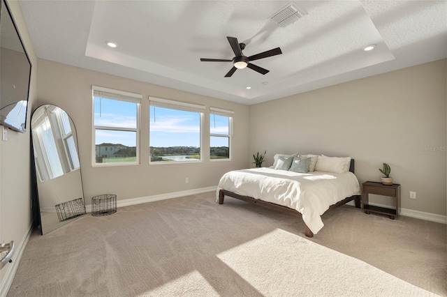 bedroom featuring ceiling fan, a tray ceiling, and light carpet