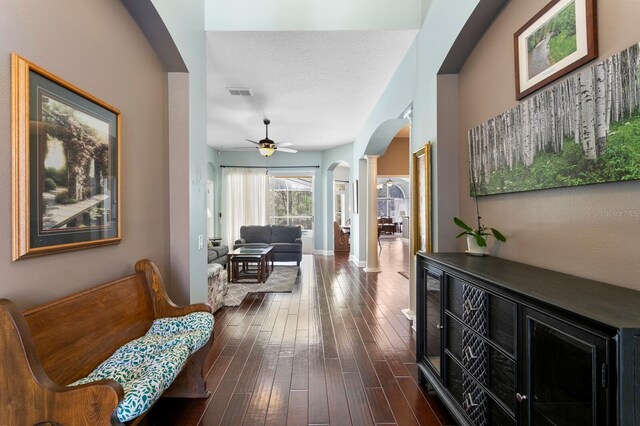 hallway featuring visible vents, baseboards, arched walkways, ornate columns, and dark wood-style flooring