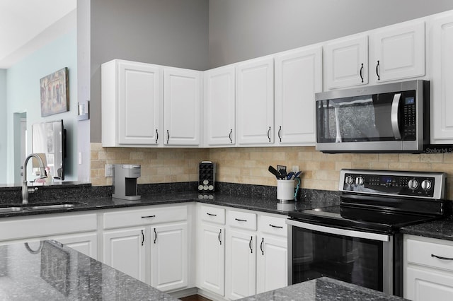 kitchen with dark stone countertops, a sink, appliances with stainless steel finishes, white cabinetry, and tasteful backsplash