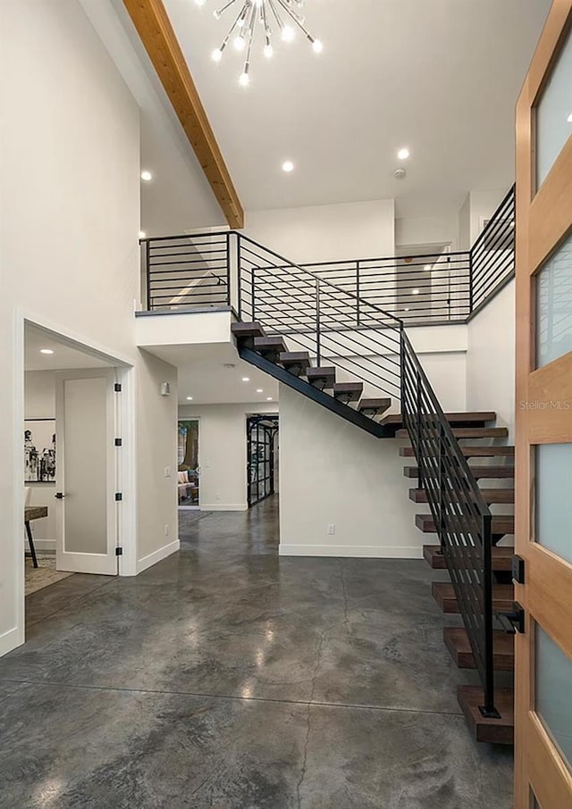 stairway with a notable chandelier, a towering ceiling, concrete floors, and beamed ceiling