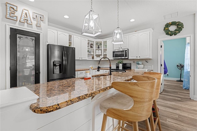 kitchen with white cabinetry, decorative light fixtures, light hardwood / wood-style flooring, dark stone counters, and stainless steel appliances