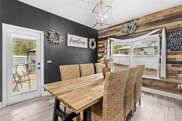 dining space with an inviting chandelier, a wealth of natural light, wood-type flooring, and wood walls