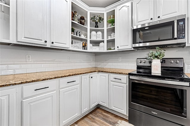 kitchen featuring stainless steel appliances, white cabinetry, hardwood / wood-style flooring, and dark stone countertops