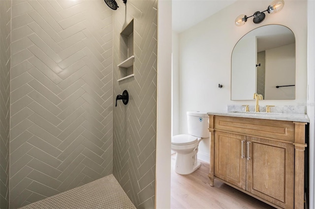 bathroom with vanity, toilet, wood-type flooring, and a tile shower