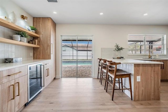 bar featuring wine cooler, sink, decorative backsplash, and light wood-type flooring