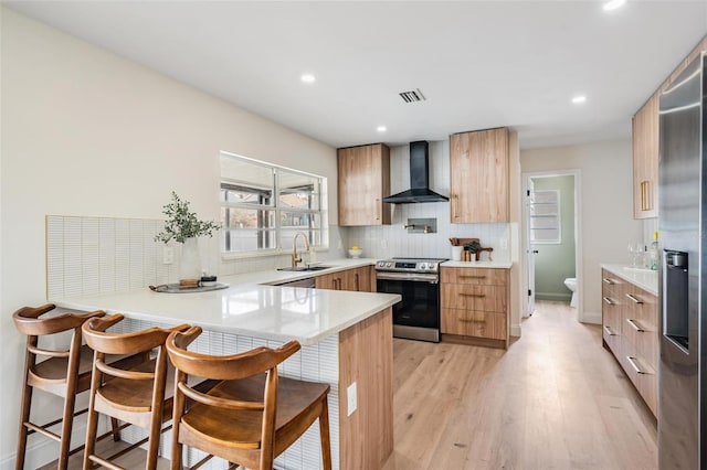 kitchen featuring sink, a kitchen breakfast bar, stainless steel appliances, kitchen peninsula, and wall chimney exhaust hood