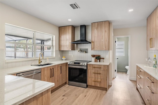 kitchen featuring wall chimney range hood, sink, appliances with stainless steel finishes, backsplash, and light stone countertops