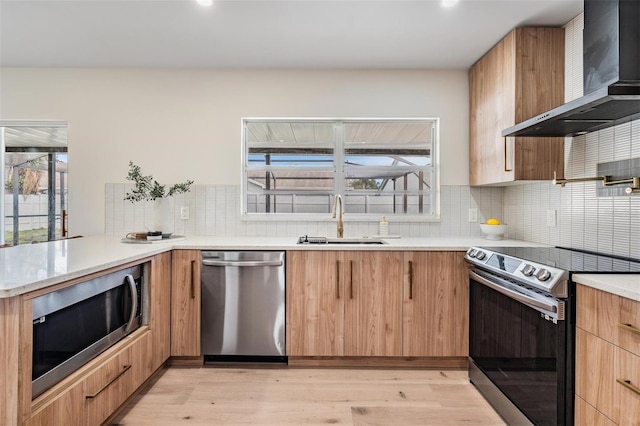 kitchen featuring wall chimney range hood, sink, stainless steel appliances, light hardwood / wood-style floors, and kitchen peninsula