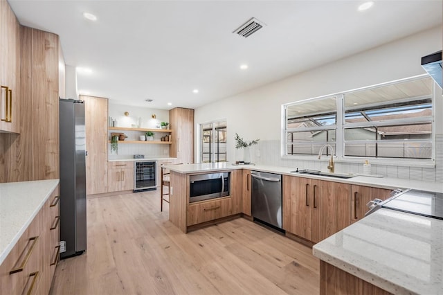 kitchen featuring sink, appliances with stainless steel finishes, wine cooler, light stone countertops, and kitchen peninsula