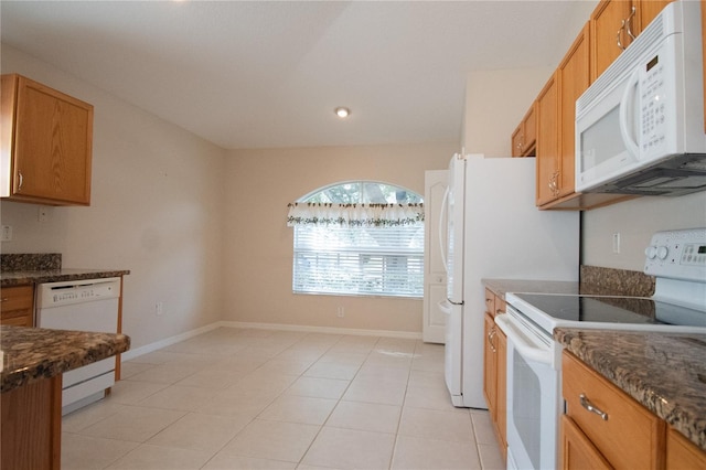 kitchen featuring light tile patterned floors, white appliances, and dark stone counters