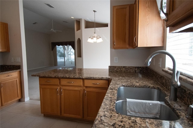 kitchen featuring sink, kitchen peninsula, pendant lighting, dark stone counters, and ceiling fan with notable chandelier