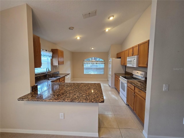 kitchen with white appliances, kitchen peninsula, sink, and dark stone countertops