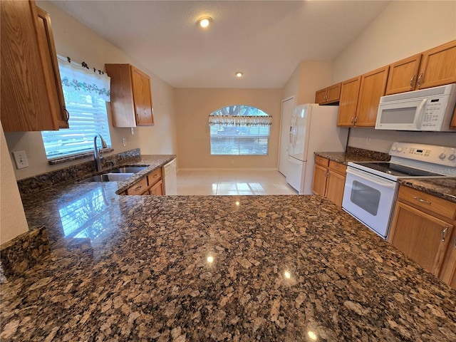 kitchen with lofted ceiling, sink, white appliances, light tile patterned floors, and dark stone countertops