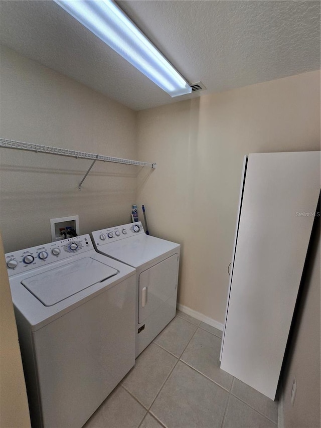 clothes washing area featuring independent washer and dryer, a textured ceiling, and light tile patterned flooring