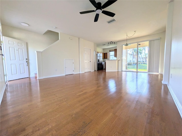 unfurnished living room featuring a ceiling fan, baseboards, visible vents, and wood finished floors