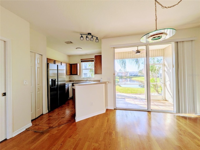 kitchen with wood finished floors, a peninsula, a water view, fridge with ice dispenser, and light countertops