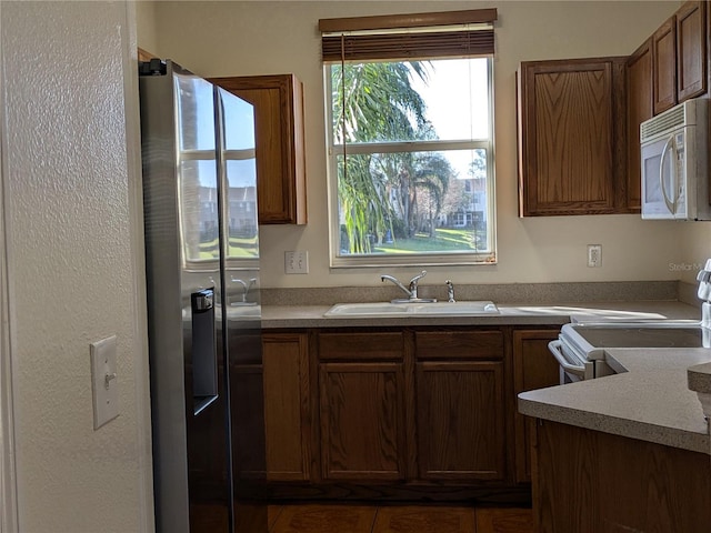 kitchen featuring light countertops, white appliances, a sink, and brown cabinets