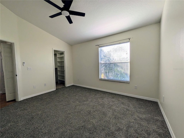 unfurnished bedroom featuring a walk in closet, dark carpet, vaulted ceiling, a textured ceiling, and baseboards