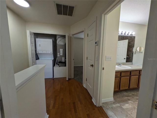 hall with a sink, light wood-style floors, visible vents, and stacked washer / drying machine