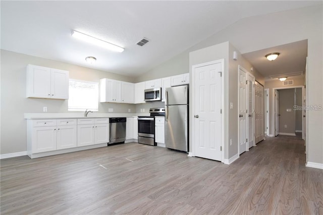 kitchen with vaulted ceiling, white cabinetry, and appliances with stainless steel finishes