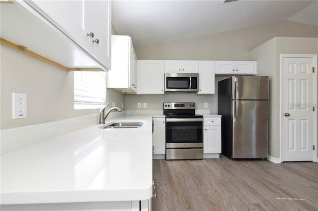 kitchen with lofted ceiling, sink, appliances with stainless steel finishes, white cabinetry, and light hardwood / wood-style floors