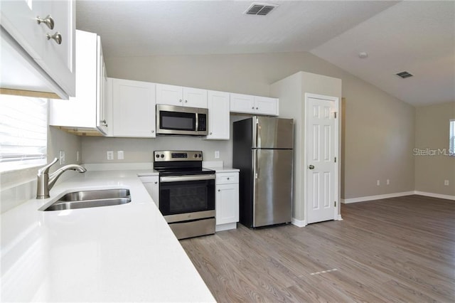 kitchen with appliances with stainless steel finishes, sink, white cabinets, and light wood-type flooring