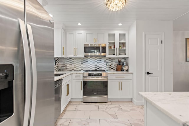 kitchen featuring white cabinetry, an inviting chandelier, stainless steel appliances, light stone counters, and tasteful backsplash