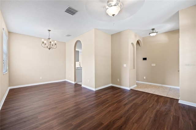 empty room with dark wood-type flooring and ceiling fan with notable chandelier