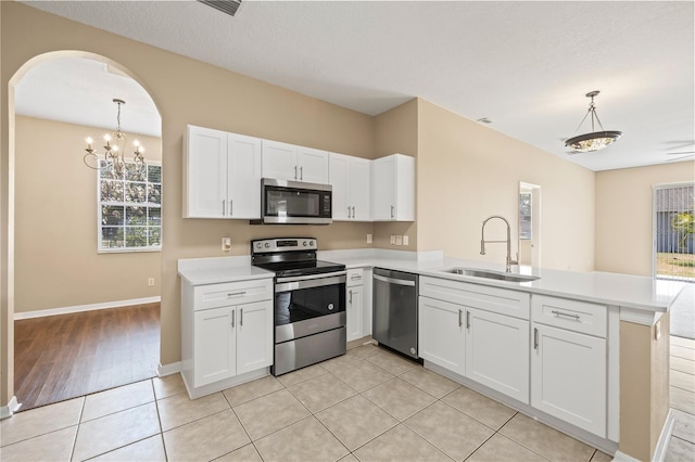 kitchen with appliances with stainless steel finishes, sink, white cabinets, hanging light fixtures, and kitchen peninsula