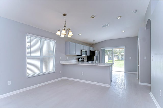 kitchen featuring lofted ceiling, hanging light fixtures, kitchen peninsula, stainless steel appliances, and an inviting chandelier