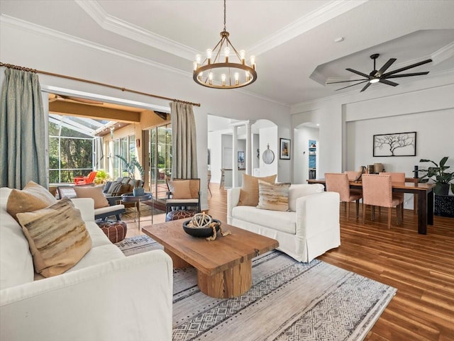 living room featuring hardwood / wood-style flooring, a tray ceiling, ceiling fan with notable chandelier, and crown molding