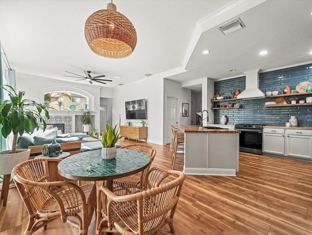 dining room with sink, crown molding, light hardwood / wood-style flooring, ceiling fan, and a tiled fireplace