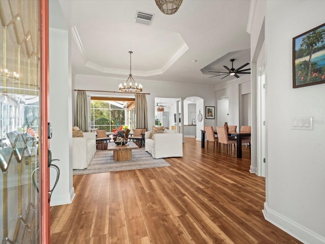 unfurnished living room with ceiling fan with notable chandelier, ornamental molding, a raised ceiling, and hardwood / wood-style flooring