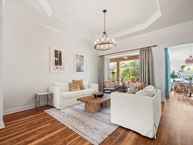 living room with crown molding, hardwood / wood-style flooring, a raised ceiling, and a chandelier