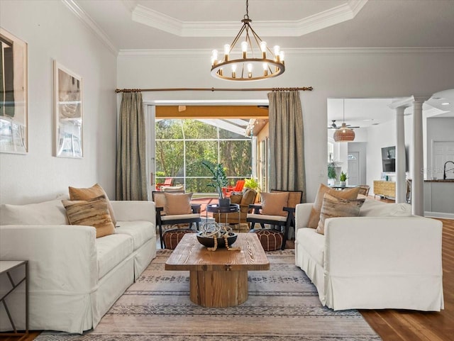 living room featuring decorative columns, a notable chandelier, wood-type flooring, ornamental molding, and a raised ceiling