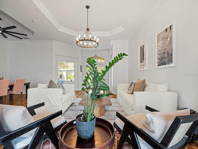 interior space with ornamental molding, ceiling fan with notable chandelier, hardwood / wood-style floors, and a tray ceiling