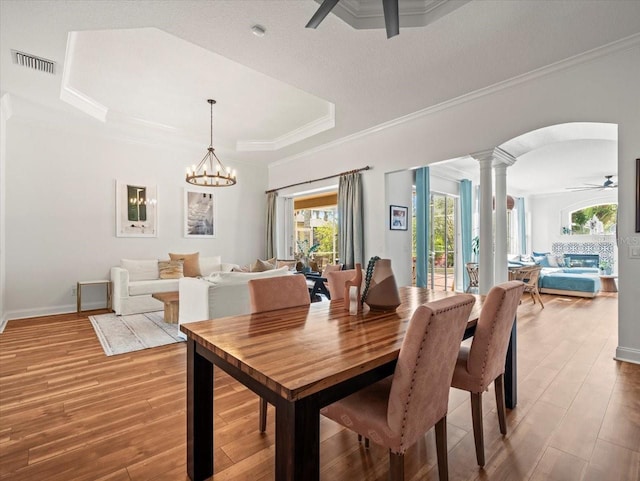 dining room featuring ornate columns, wood-type flooring, ornamental molding, a tray ceiling, and ceiling fan with notable chandelier