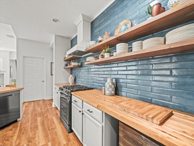 kitchen featuring butcher block countertops, stainless steel gas range, black dishwasher, light hardwood / wood-style floors, and white cabinets