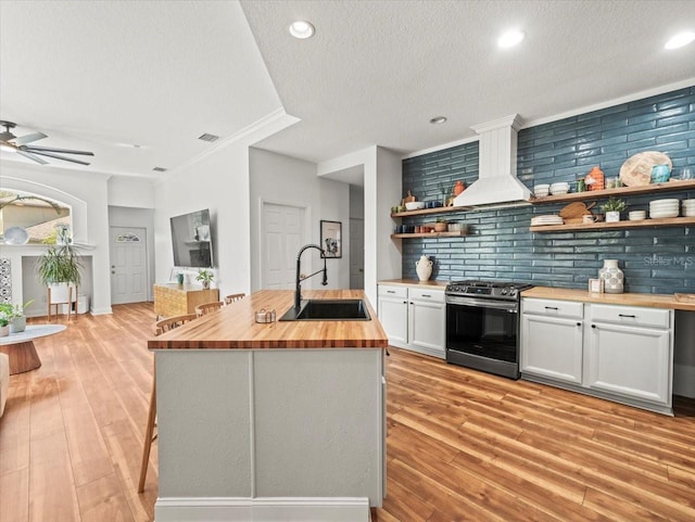 kitchen with butcher block counters, sink, a center island with sink, stainless steel electric range, and white cabinets