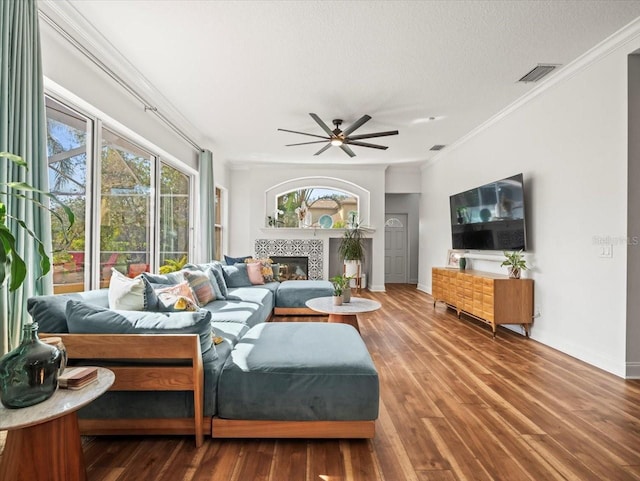 living room with crown molding, hardwood / wood-style flooring, ceiling fan, a fireplace, and a textured ceiling