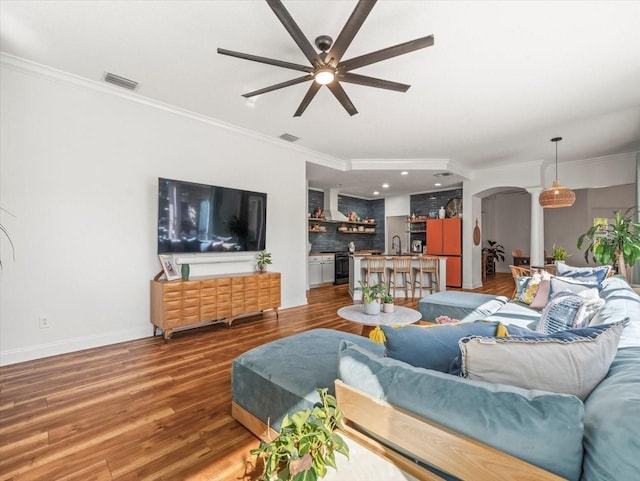 living room featuring hardwood / wood-style flooring, ceiling fan, ornamental molding, and indoor wet bar