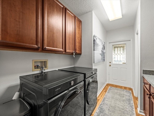 clothes washing area with cabinets, a textured ceiling, washer and clothes dryer, and light hardwood / wood-style flooring