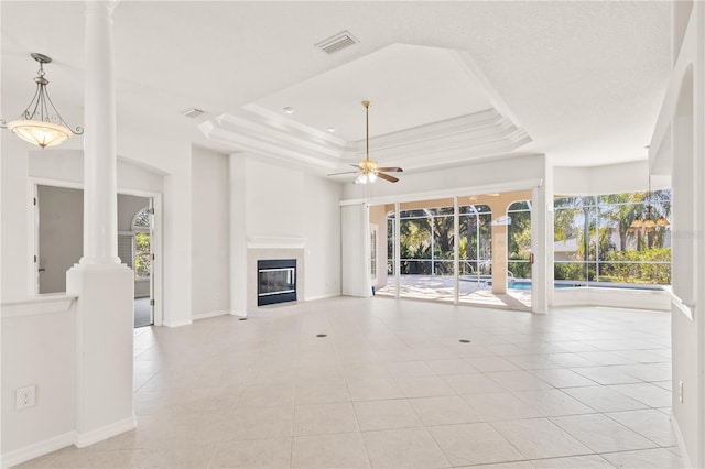 unfurnished living room with light tile patterned floors, a tray ceiling, ceiling fan, and ornate columns