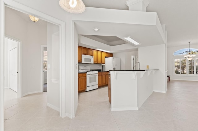 kitchen with light tile patterned floors, a tray ceiling, kitchen peninsula, a notable chandelier, and white appliances