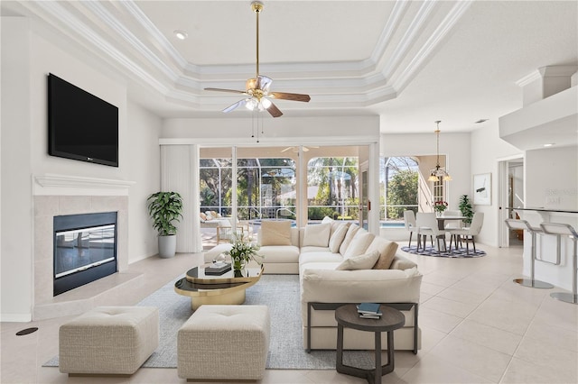 living room featuring a tile fireplace, ornamental molding, light tile patterned flooring, and a tray ceiling