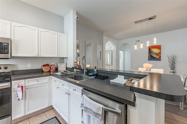 kitchen featuring pendant lighting, sink, appliances with stainless steel finishes, white cabinets, and kitchen peninsula