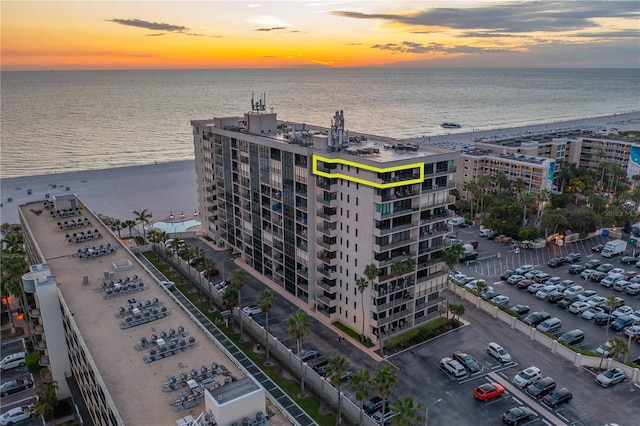 aerial view at dusk featuring a water view and a beach view