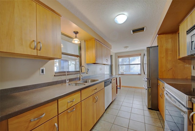 kitchen with sink, stainless steel appliances, a textured ceiling, light tile patterned flooring, and light brown cabinetry